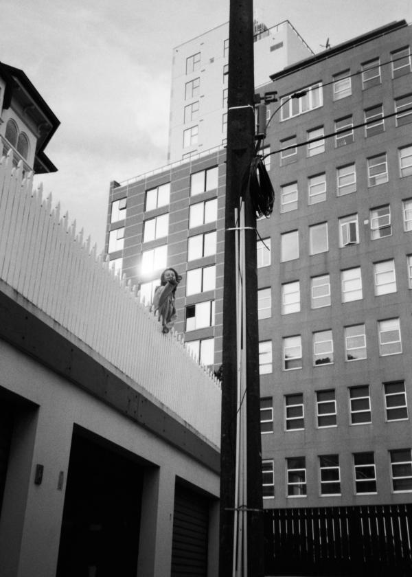 Black and white image of young woman reaching out to the photographer in a gesture of friendship. Sun burst on window of building behind subject.
