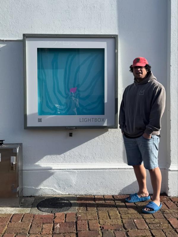 Louis Mikaere stands next to his Lightbox artwork during the day