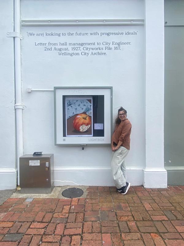 Emma Lahood stands with her playful lightbox illustration, Nibbled Edges, showing a slightly nibbled red apple