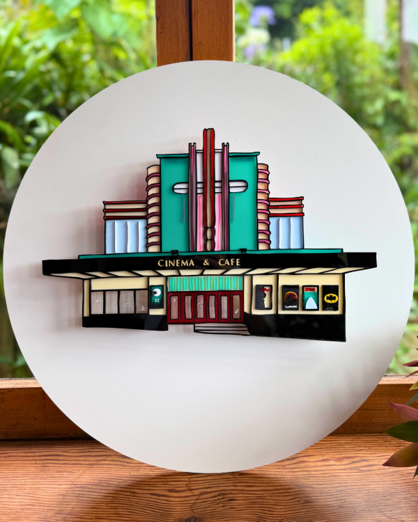 A replication of The Penthouse Cinema made of acrylic is secured onto a white circular backing 