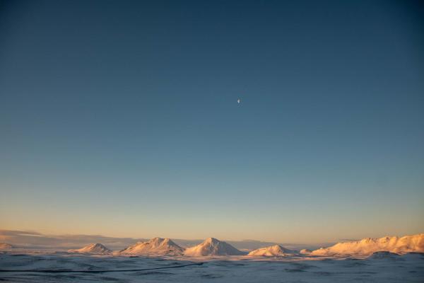 Hang The Moon by Caelyn Daughney is a photograph mostly of a blue sky, with a very small moon. At the bottom there is a clear snowy mountain range