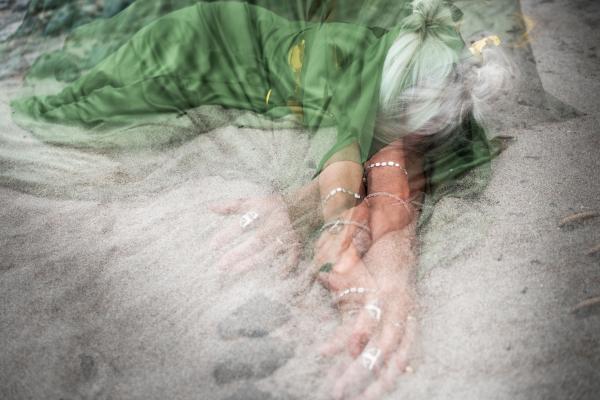 A layered photograph depicting a woman with white hair and a green dress lying in the sand