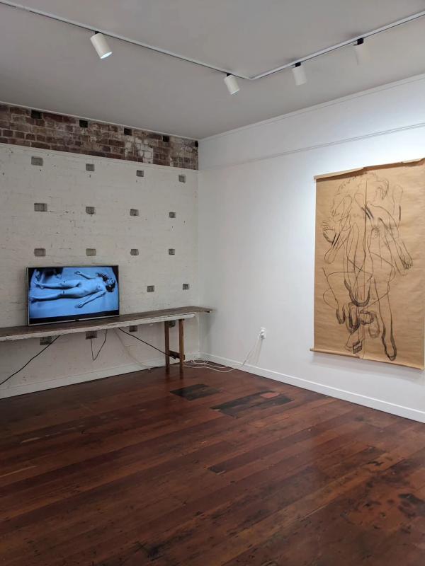 Installation view of video and life-sized drawing of nude artist.