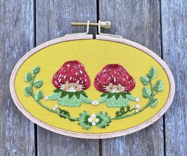 Embroidery by Rae Huang. A pair of cute cats with strawberry hats, enclosed in a garland.