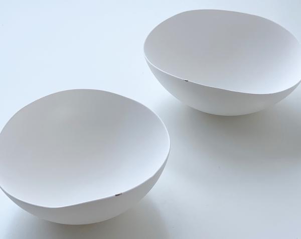 Two handmade minimalist bowls made by Kimiko Suzuki. They are white with a slightly off-centre curve to them, and a tiny patch of gold