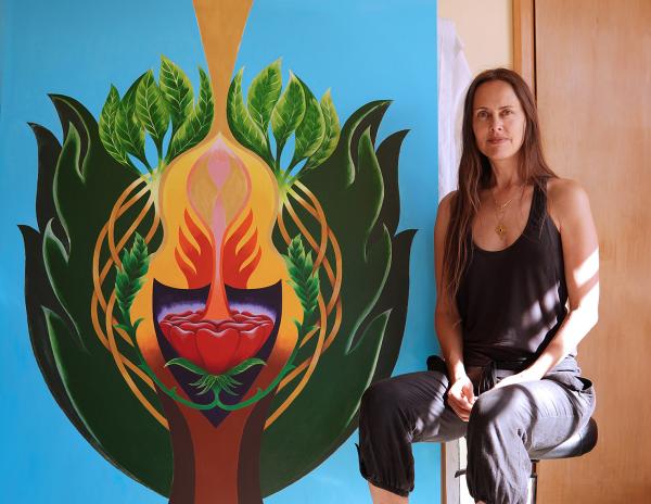 Emily Fletcher sits with her painting The Tree of Protection, a large abstract painting of a tree on a blue background